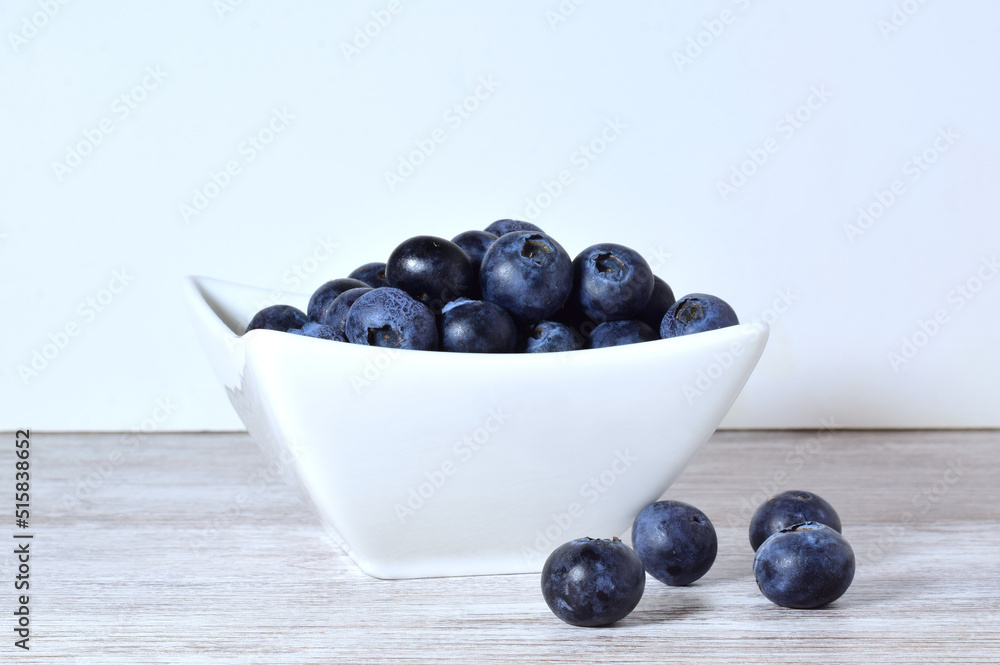 Blueberries in porcelain bowl and scattered on the table. Blueberries in porcelain bowl and scattered on the table.