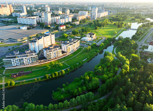 Townhouses and multi-floor home near river. River in city on sunrise, aerial view. Suburb houses and multi-storey residential buildings near river. Cottages and wooden suburb house. Lake in town.