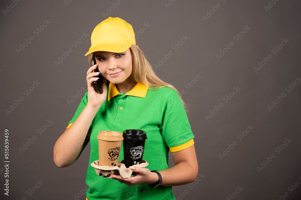 Young deliverywoman with cups of coffee speaking on smartphone Young deliverywoman with cups of coffee speaking on smartphone