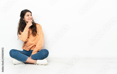 Teenager Russian girl sitting on the floor looking to the side and smiling