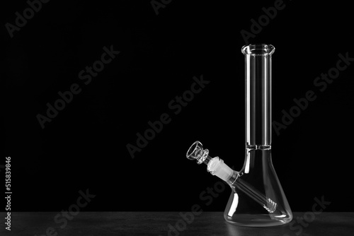 Photos Glass bong on grey table against black background, space for text