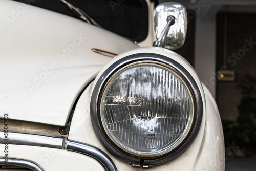 Round headlight of a white old timer car. Close up