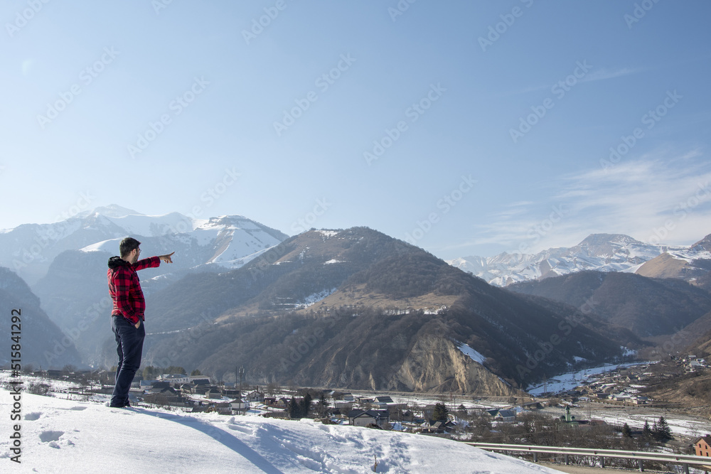 A man stands holding a remote control from a drone against the backdrop of mountains
