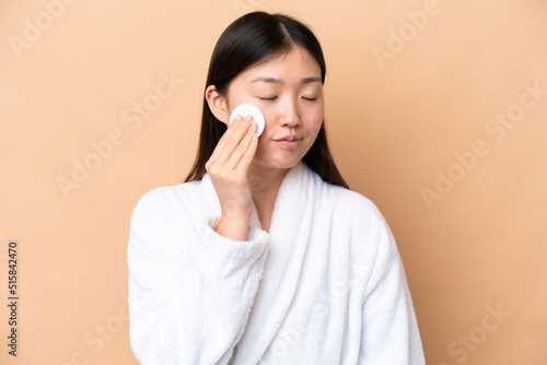 Young Chinese woman isolated on beige background with cotton pad for removing makeup from her face