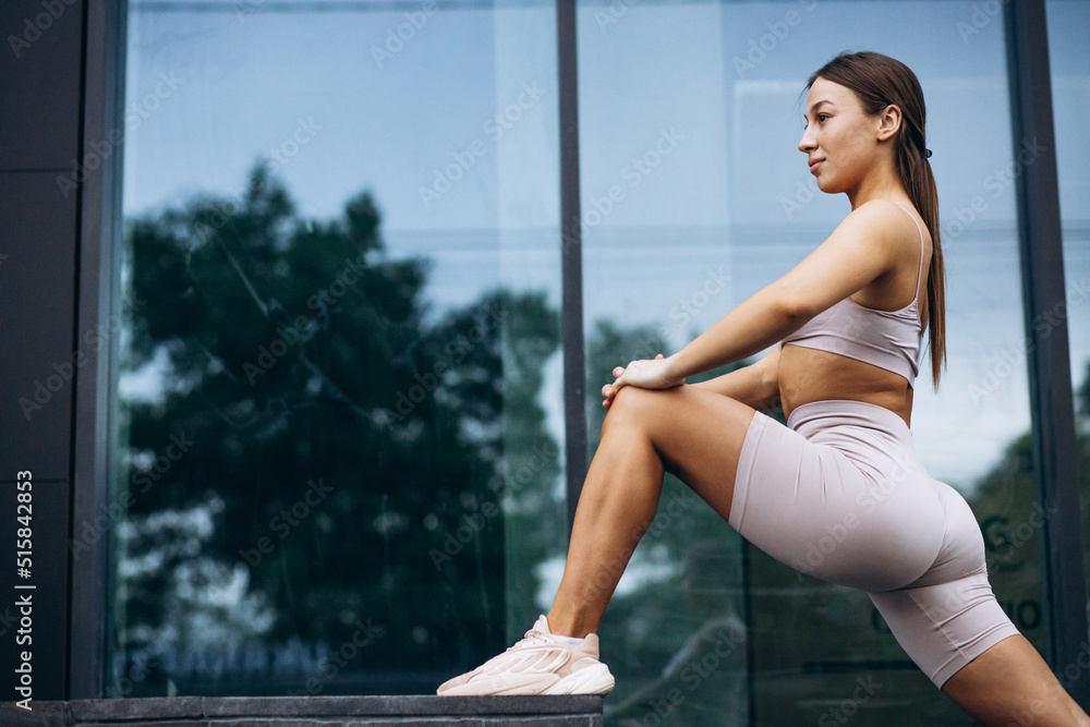 Woman fitness instructor stretching by the building