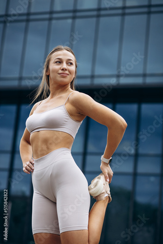 Woman fitness instructor stretching by the building