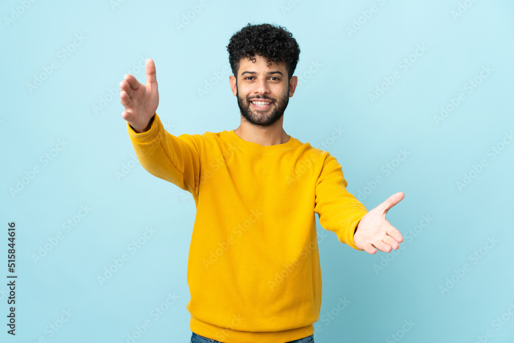Young Moroccan man isolated on blue background presenting and inviting to come with hand Young Moroccan man isolated on blue background presenting and inviting to come with hand