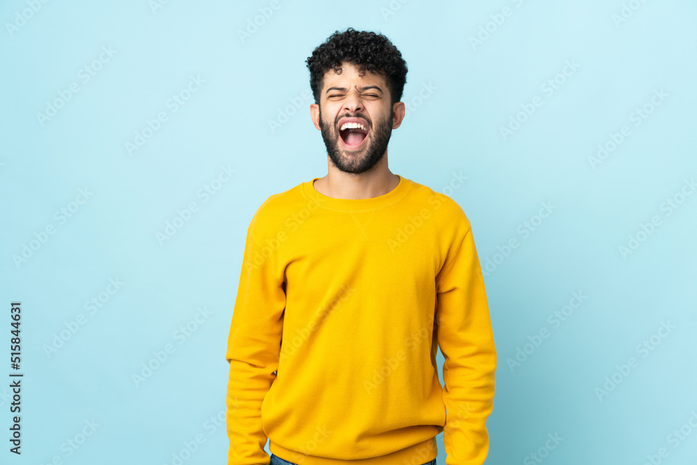 Young Moroccan man isolated on blue background shouting to the front with mouth wide open Young Moroccan man isolated on blue background shouting to the front with mouth wide open