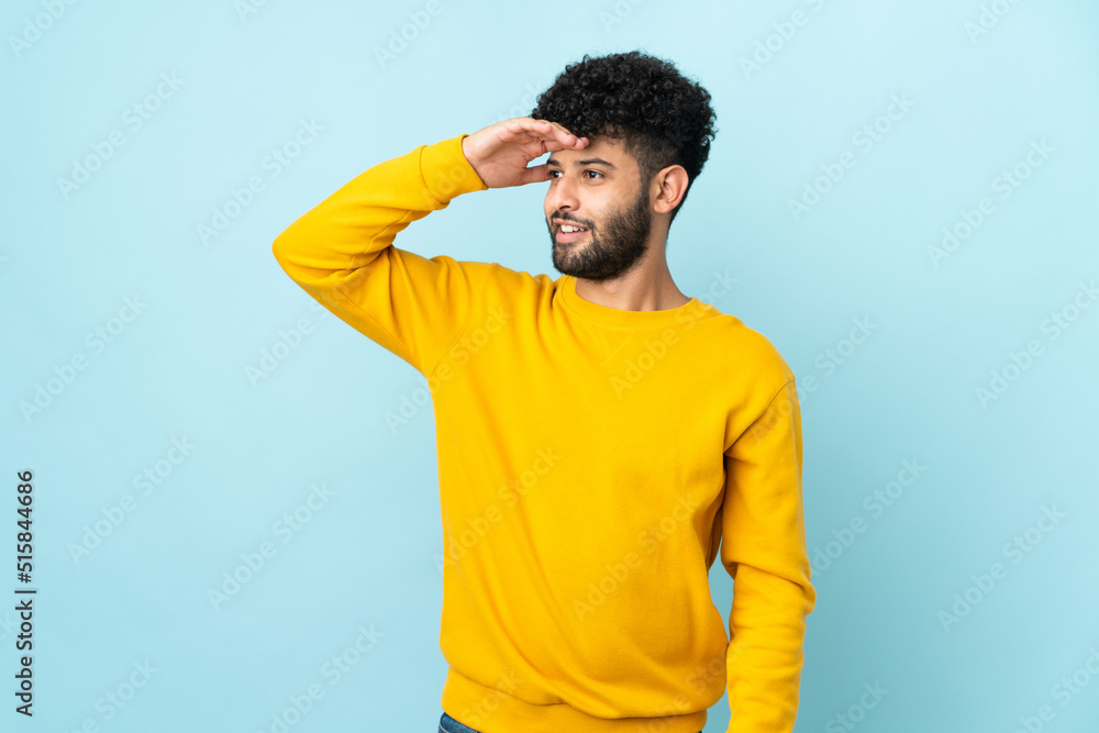 Young Moroccan man isolated on blue background with surprise expression while looking side Young Moroccan man isolated on blue background with surprise expression while looking side