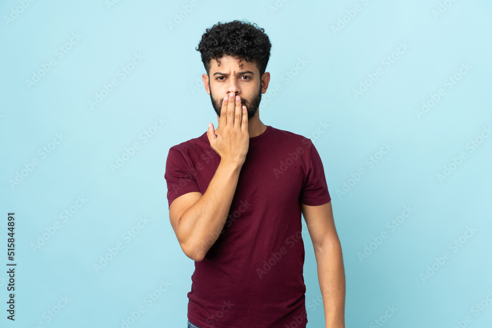 Young Moroccan man isolated on blue background covering mouth with hand Young Moroccan man isolated on blue background covering mouth with hand