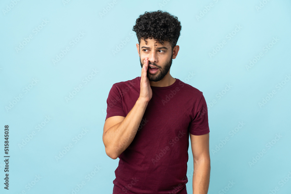 Young Moroccan man isolated on blue background whispering something with surprise gesture while looking to the side Young Moroccan man isolated on blue background whispering something with surprise gesture while looking to the side