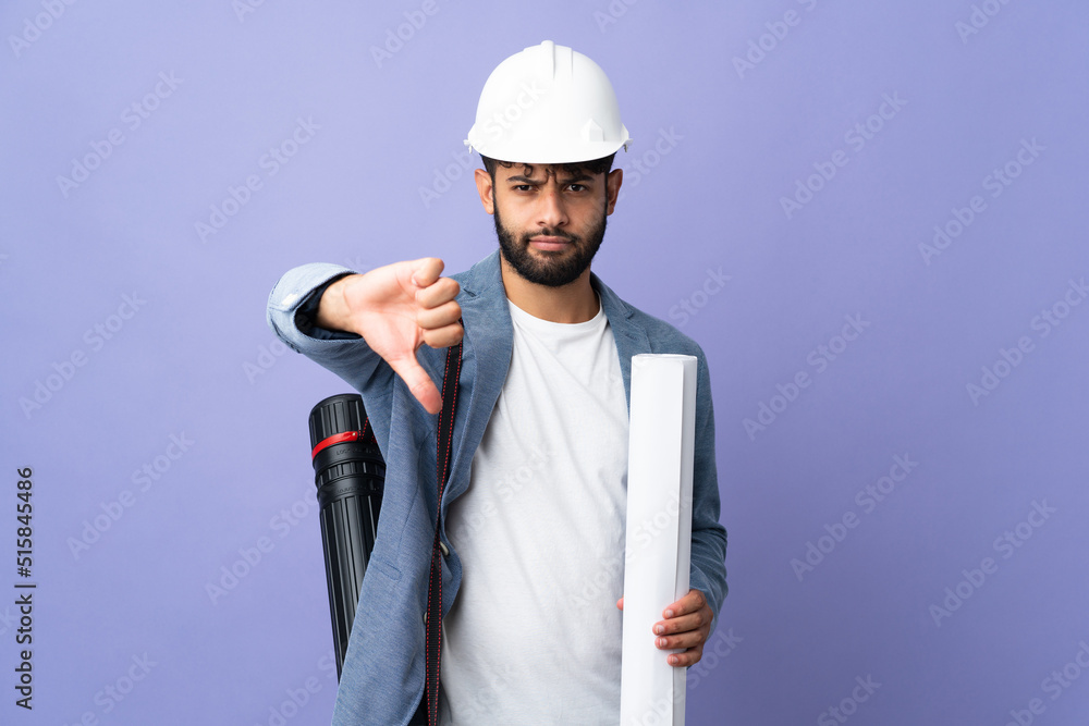 Young architect Moroccan man with helmet and holding blueprints over isolated background showing thumb down with negative expression Young architect Moroccan man with helmet and holding blueprints over isolated background showing thumb down with negative expression