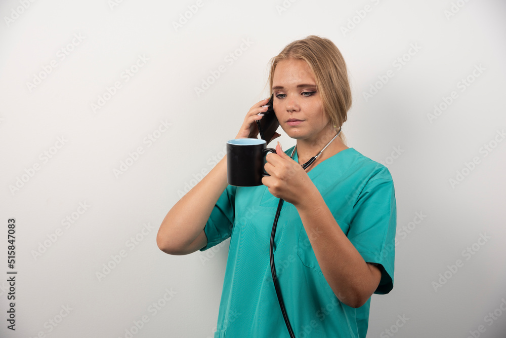 Woman doctor holding tea while talking with telephone Woman doctor holding tea while talking with telephone