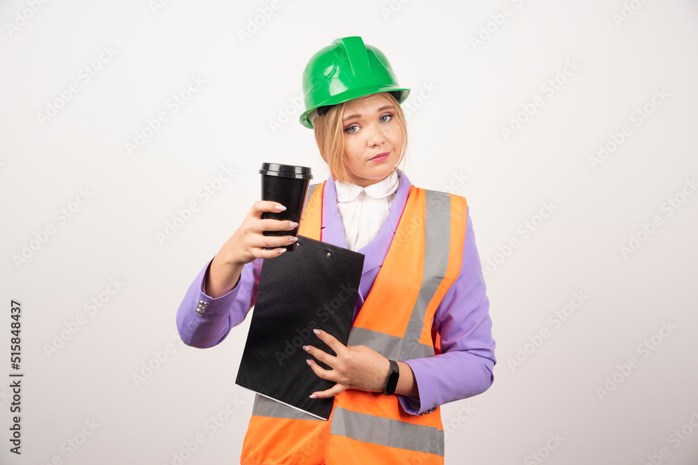 Young female industrial engineer in uniform with clipboard and black cup on white background Young female industrial engineer in uniform with clipboard and black cup on white background
