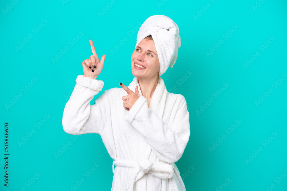 Young woman in a bathrobe isolated on blue background pointing with the index finger a great idea