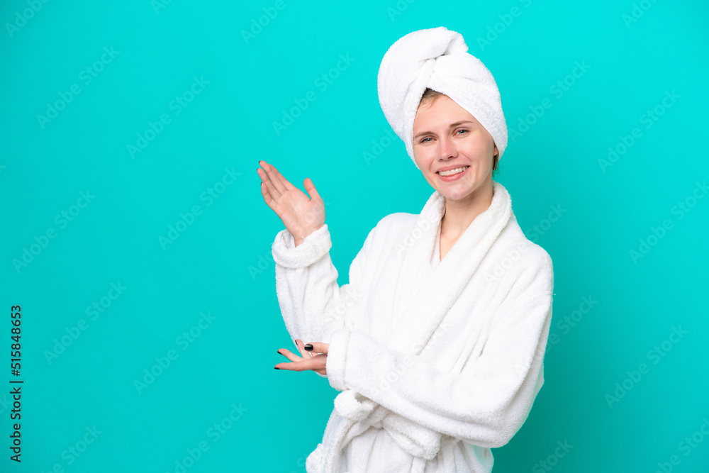 Young woman in a bathrobe isolated on blue background extending hands to the side for inviting to come Young woman in a bathrobe isolated on blue background extending hands to the side for inviting to come
