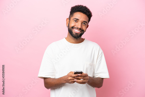 Young Brazilian man isolated on pink background sending a message with the mobile © luismolinero