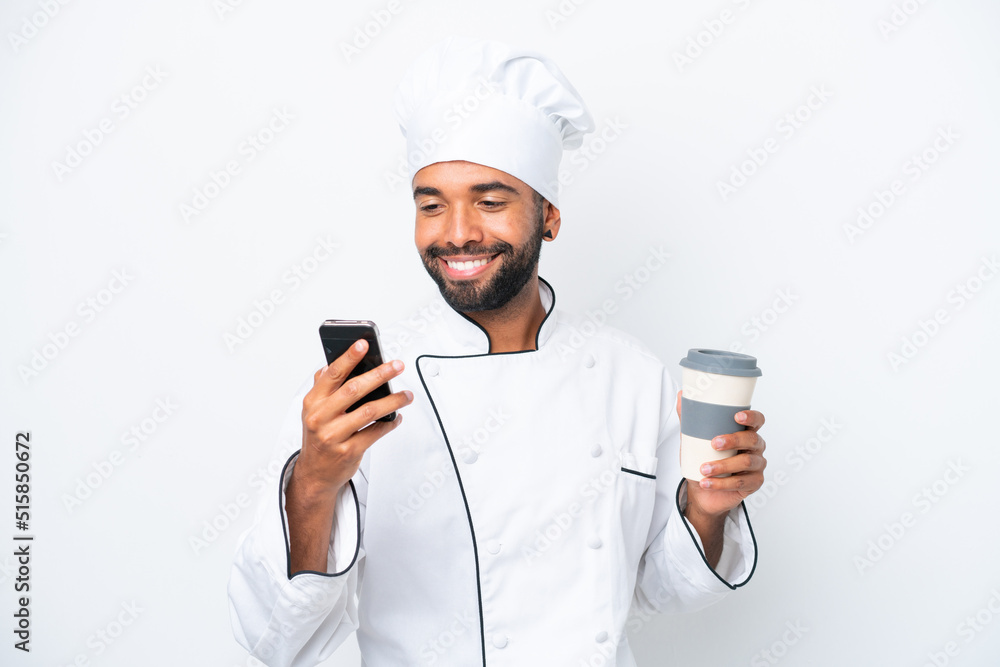 Young Brazilian chef man isolated on white background holding coffee to take away and a mobile Young Brazilian chef man isolated on white background holding coffee to take away and a mobile