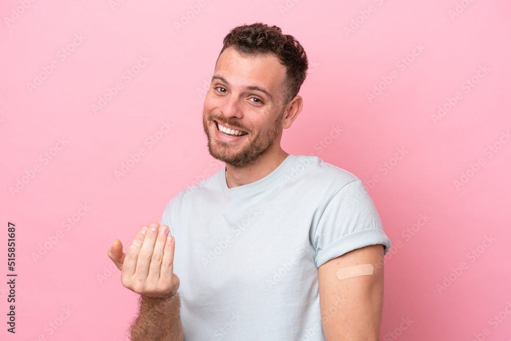 Young Brazilian man wearing a band-aids isolated on pink background inviting to come with hand. Happy that you came Young Brazilian man wearing a band-aids isolated on pink background inviting to come with hand. Happy that you came