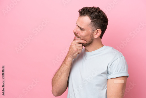 Young Brazilian man wearing a band-aids isolated on pink background thinking an idea and looking side