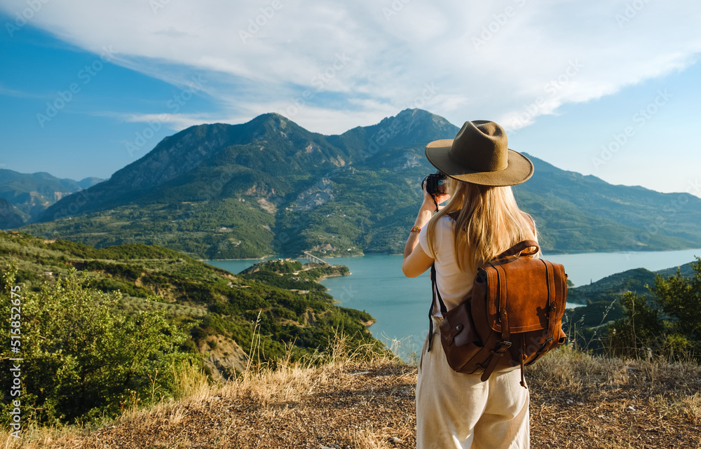 Woman photographer with big backpack taking photo of mountains and blue lake. Travel and hobby concept - obrazy, fototapety, plakaty 