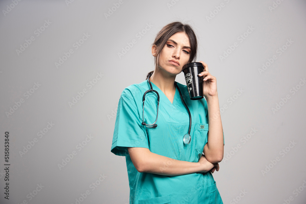 Female doctor posing with cup of coffee on gray background Female doctor posing with cup of coffee on gray background