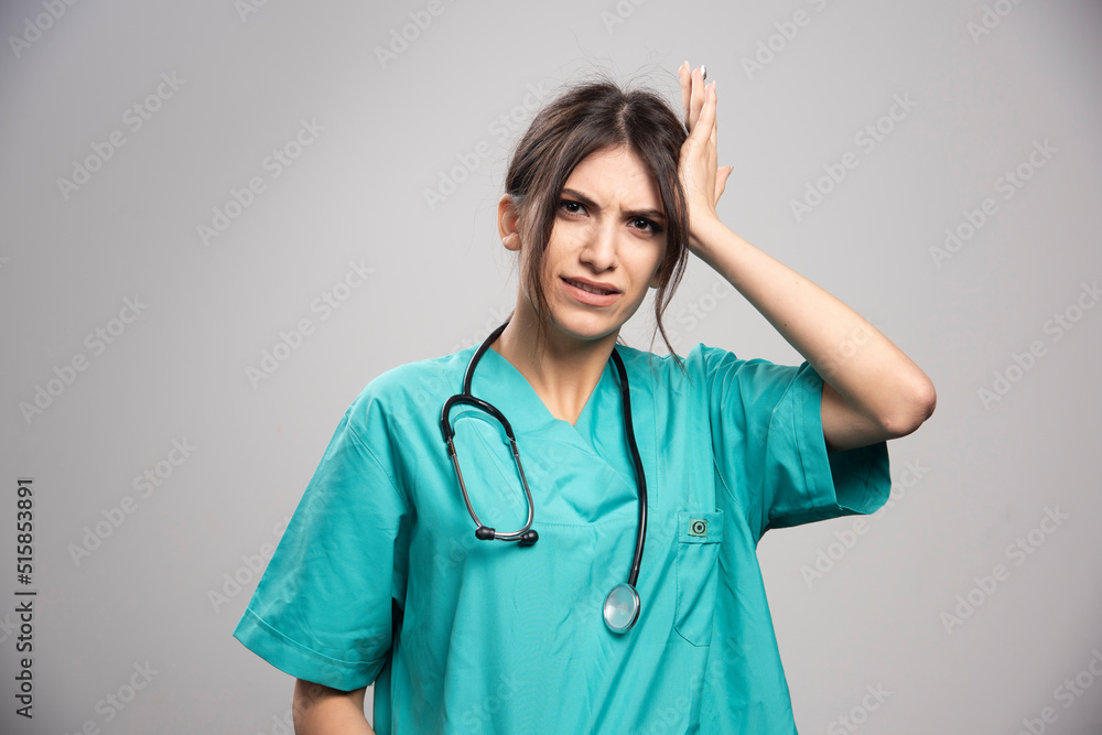 Female doctor in uniform holding her head on gray background Female doctor in uniform holding her head on gray background