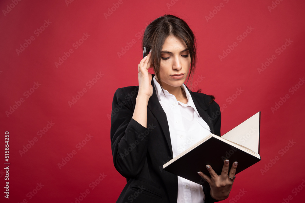 Successful employee reading her memory book on red background Successful employee reading her memory book on red background
