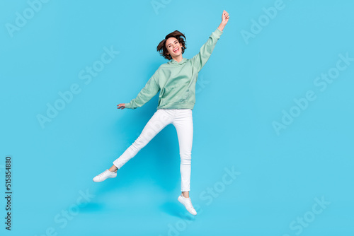 Full body photo of cool young brunette lady jump wear hoodie pants sneakers isolated on blue background
