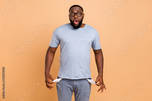 Portrait of attractive worried nervous guy showing empty pockets oops isolated over beige pastel color background