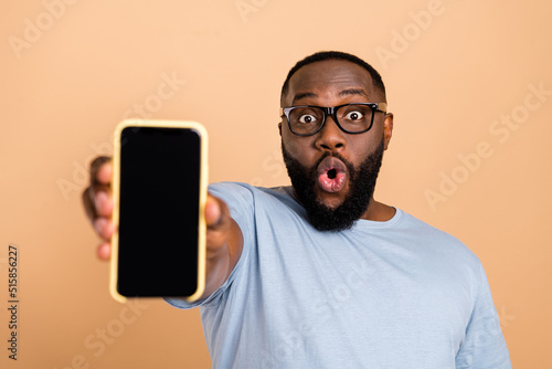 Photo of impressed young beard guy show telephone wear eyewear blue outfit isolated on beige color background