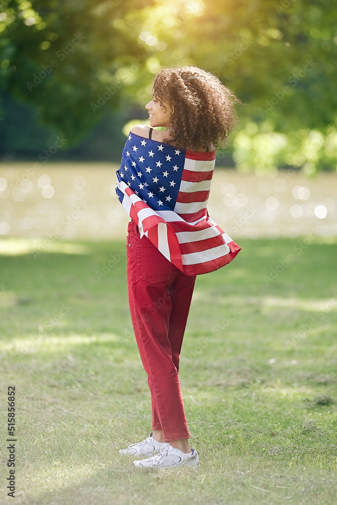 Young African american woman at nature background with an American USA flag on her shoulders. USA resident, US citizen. Immigration concept	