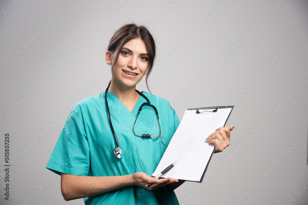 Young female doctor holding clipboard on gray background Young female doctor holding clipboard on gray background