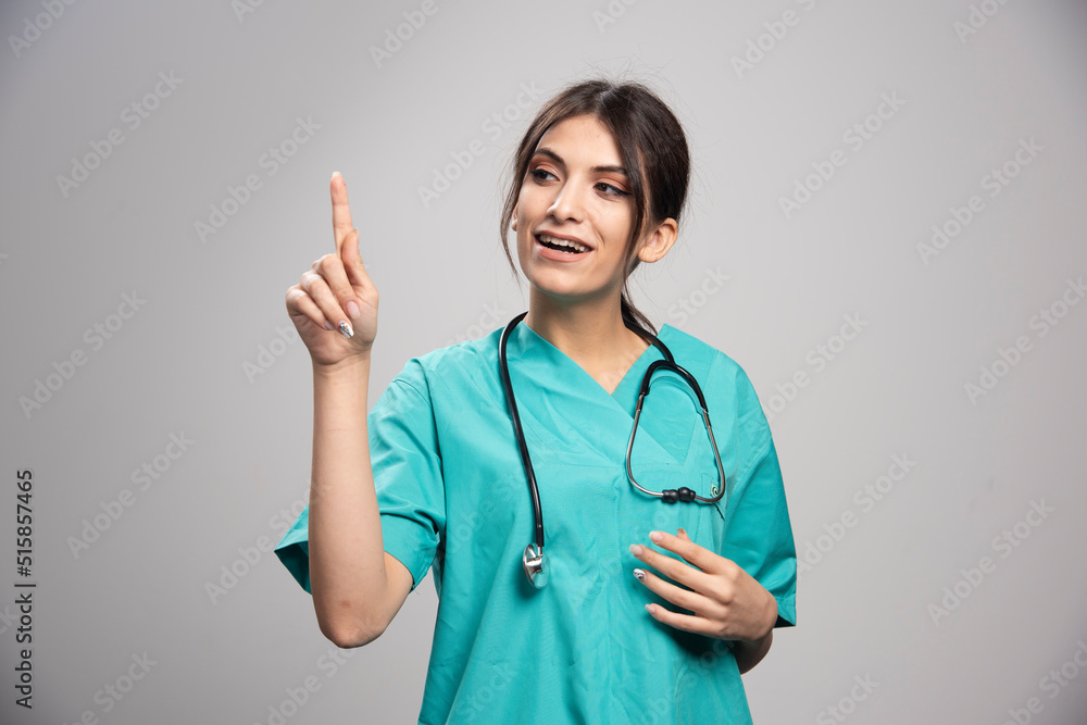 Beautiful doctor pointing at something on gray background Beautiful doctor pointing at something on gray background