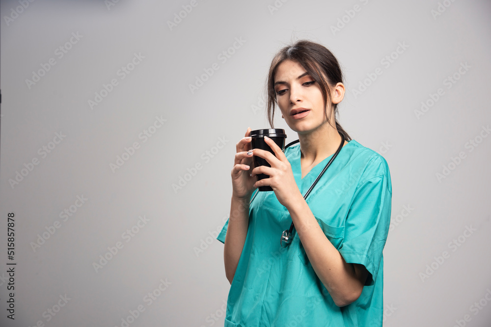 Female doctor smells aroma of coffee on gray background Female doctor smells aroma of coffee on gray background
