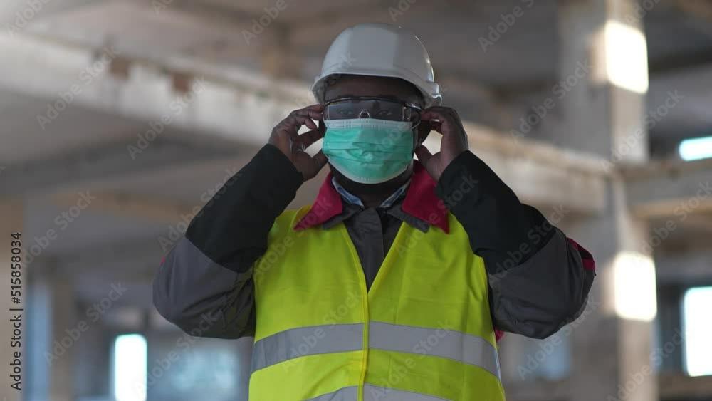 African american builder at construction site put on medical protective mask and folded his arms across his chest African american builder at construction site put on medical protective mask and folded his arms across his chest