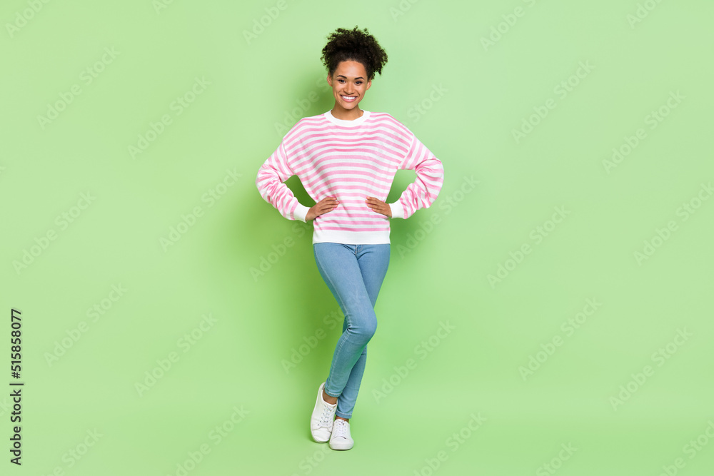 Photo of positive charming lady hands hips shiny smile wear striped shirt jeans isolated green color background Photo of positive charming lady hands hips shiny smile wear striped shirt jeans isolated green color background