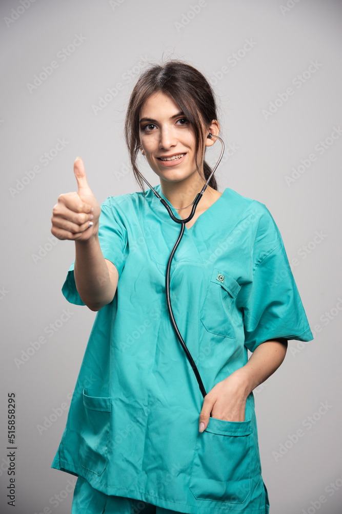 Female doctor with stethoscope giving thumbs up on gray background Female doctor with stethoscope giving thumbs up on gray background