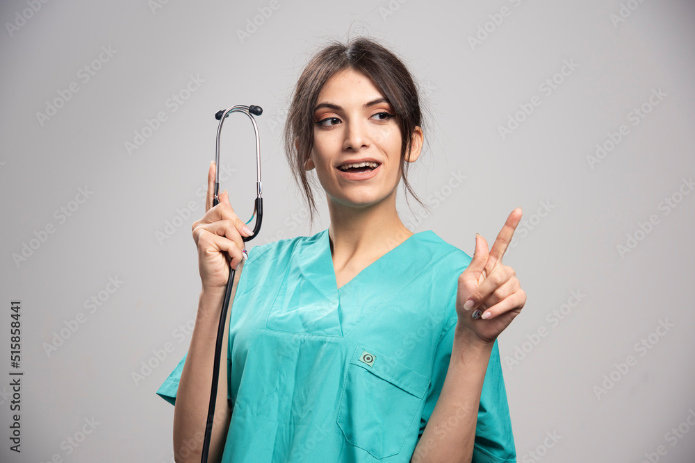 Happy doctor showing stethoscope on gray background Happy doctor showing stethoscope on gray background