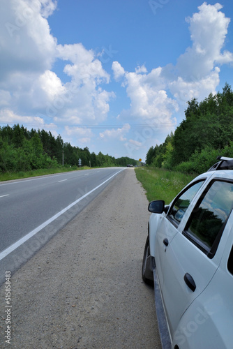 The car is parked on the side of a country road on a summer day