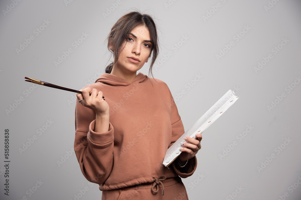 Fototapeta premium Young woman holding paint brushes and canvas