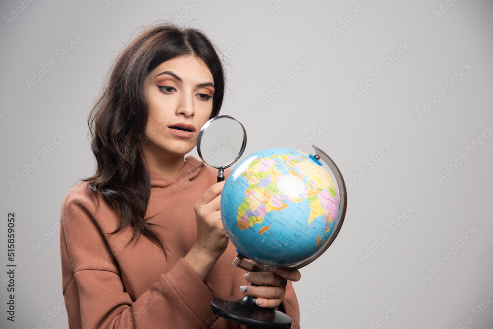 Brunette woman looking at globe with magnifying glass Brunette woman looking at globe with magnifying glass