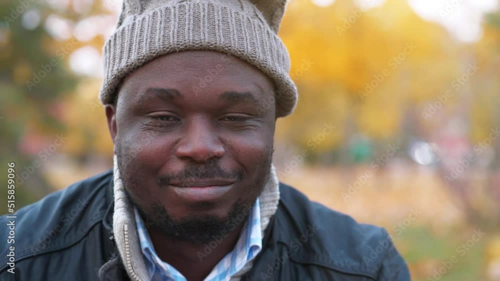 Adult african american man in winter hat with sad smile looks at camera, close-up shot Adult african american man in winter hat with sad smile looks at camera, close-up shot