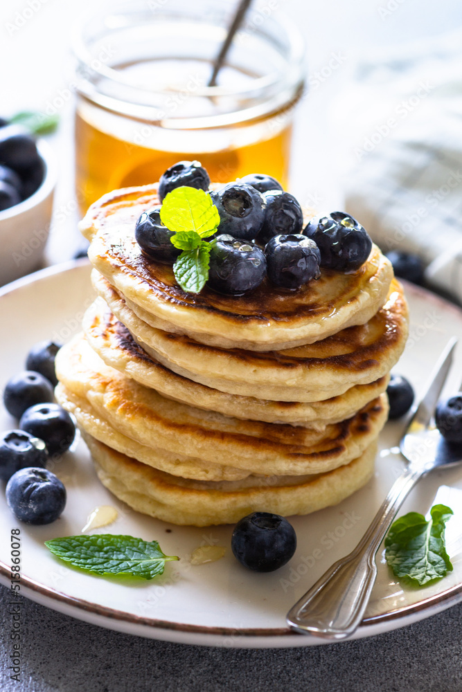 Pancakes stack with fresh blueberries and honey at white stone table. Pancakes stack with fresh blueberries and honey at white stone table.