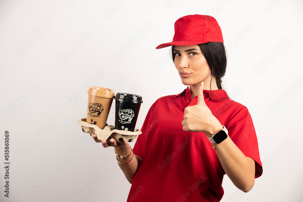 Female courier in uniform holding coffees and showing thumbs up Female courier in uniform holding coffees and showing thumbs up