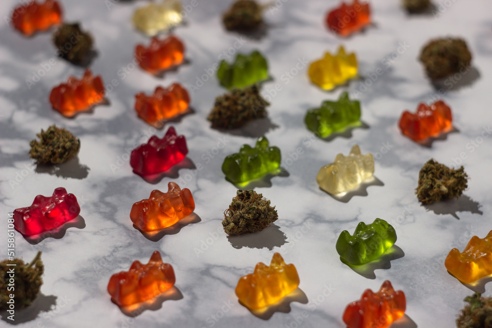 Several dry buds of medical marijuana lie in order among gummy bears of different colors with the addition of cbd oil on a marble table, Making up a pattern Several dry buds of medical marijuana lie in order among gummy bears of different colors with the addition of cbd oil on a marble table, Making up a pattern