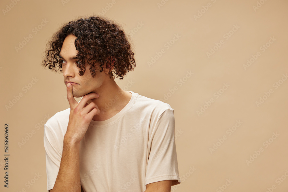 Pensive funny awesome tanned curly man in basic t-shirt can not make decision posing isolated on beige pastel background. Fashion New Collection offer. People and Emotions concept. Free place for ad Pensive funny awesome tanned curly man in basic t-shirt can not make decision posing isolated on beige pastel background. Fashion New Collection offer. People and Emotions concept. Free place for ad