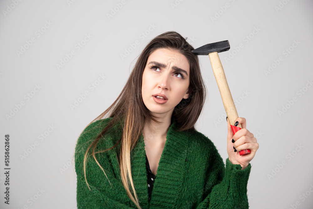 Pensive woman holding hammer in hands on a gray background Pensive woman holding hammer in hands on a gray background