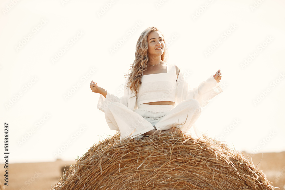 Naklejka premium Beautiful young woman in vwhite dress sitting on hay bale.