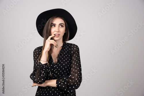 Beautiful woman in black hat standing on gray background